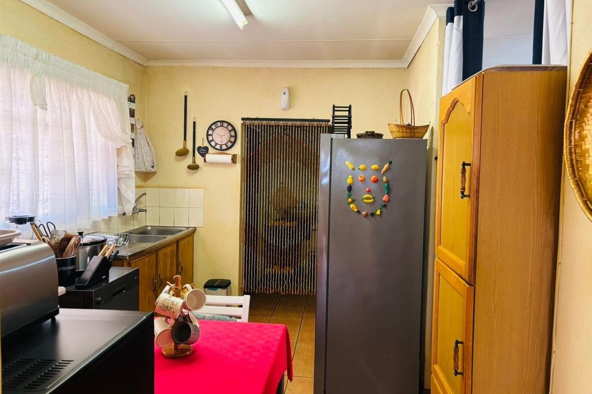 A functional kitchen featuring built-in wooden cabinetry, a stainless steel sink, and tiled flooring, offering potential for a modern renovation.