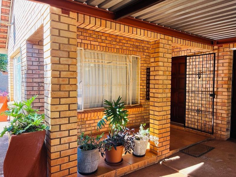 A covered patio area featuring face brick pillars, tiled flooring, and a corrugated metal roof, providing a sheltered entrance to the home.