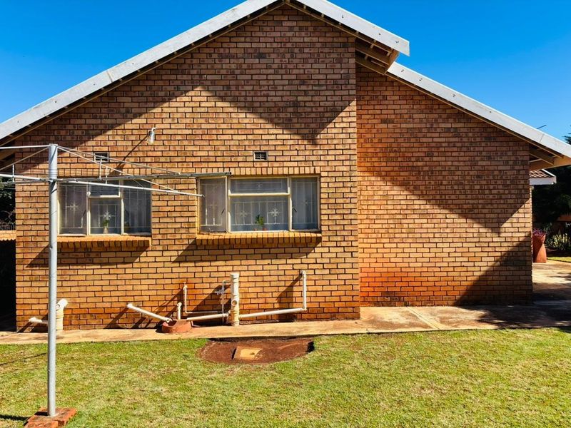 Rear view of a face brick house featuring a metal roof and steel frame windows with visible external plumbing infrastructure.