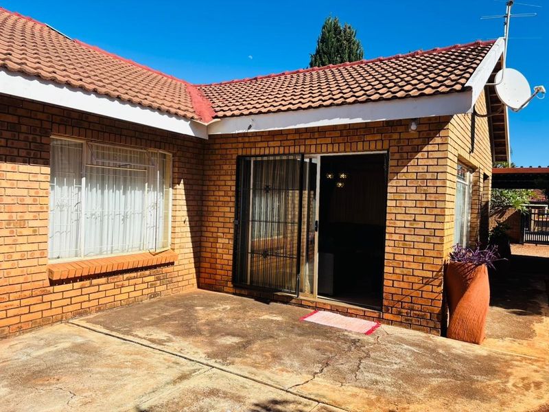 Rear exterior view of the house featuring a face brick facade, tiled roof, and a concrete patio area with a sliding glass door entrance.