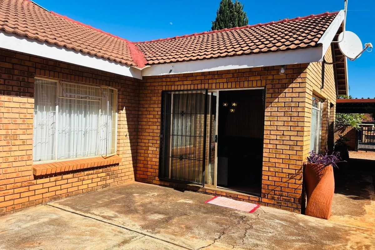 Rear exterior view of the house featuring a face brick facade, tiled roof, and a concrete patio area with a sliding glass door entrance.