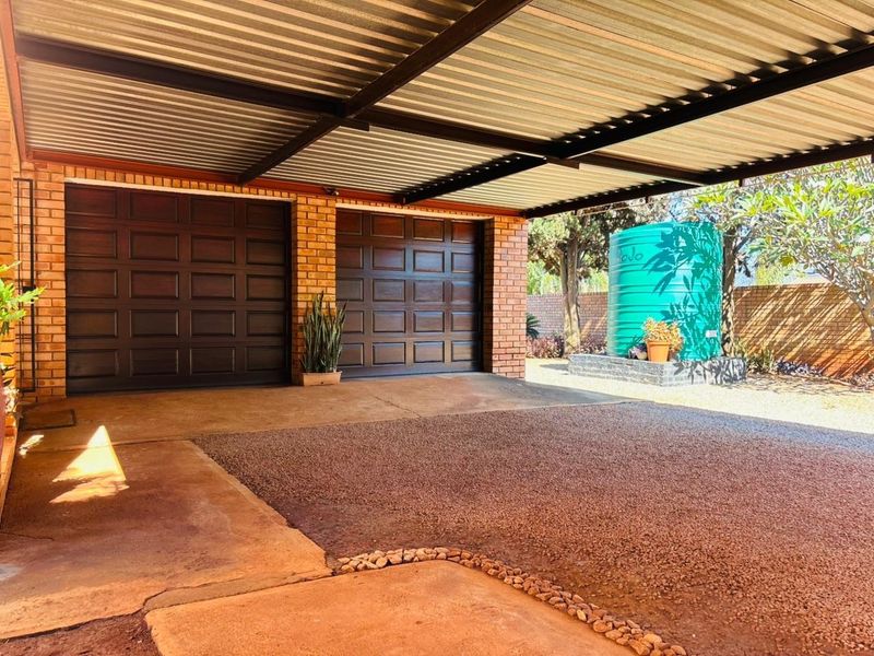 A covered double garage area featuring brick construction, corrugated roofing, and an adjacent water storage tank on a concrete driveway.