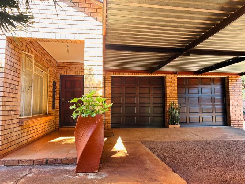 Front elevation featuring a face brick facade, double garage with timber doors, a covered carport, and a tiled entrance porch.
