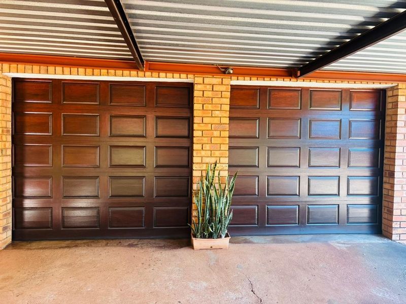 A double garage featuring dark wood-finish sectional doors, brick support pillars, and a corrugated metal roof structure.