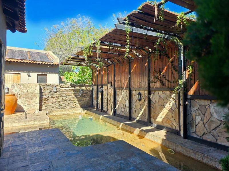 Outdoor pool area featuring a stone-clad wall, timber pergola structure, and paved surround, offering a rustic entertainment space.