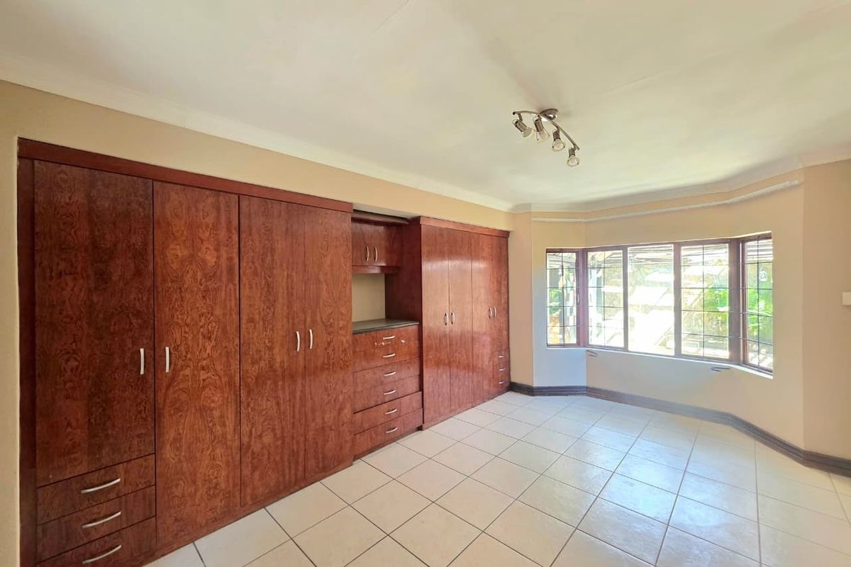 Spacious bedroom featuring extensive built-in wooden cabinetry, large bay windows providing natural light, and neutral tiled flooring throughout.