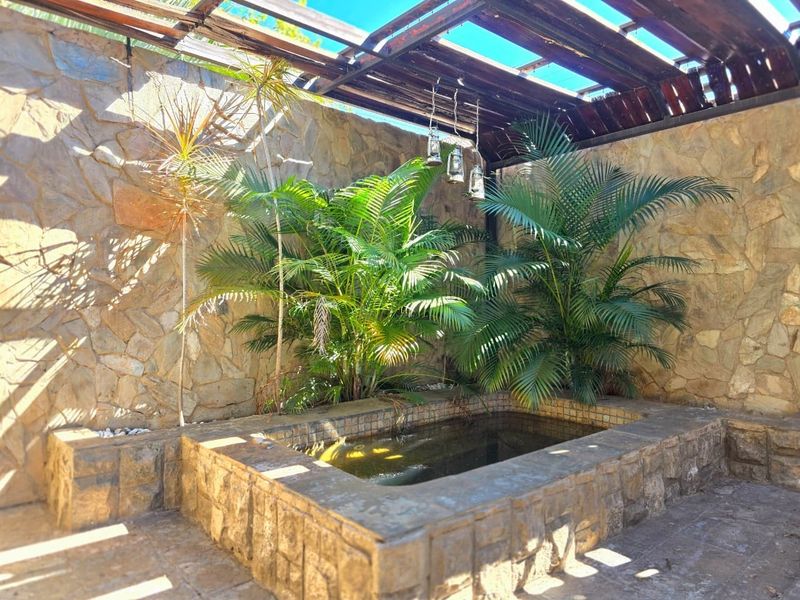 A private outdoor plunge pool area featuring natural stone walls, a timber pergola structure, and established tropical landscaping.