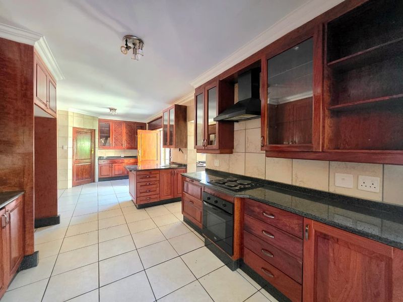 Spacious kitchen featuring extensive wooden cabinetry, granite countertops, built-in oven, gas hob, and tiled flooring throughout.