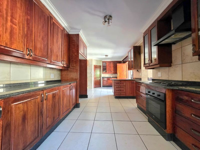 Spacious kitchen featuring extensive built-in wooden cabinetry, granite countertops, integrated oven, and hob, with neutral tiled flooring throughout.
