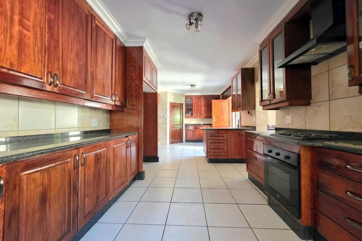 Spacious kitchen featuring extensive built-in wooden cabinetry, granite countertops, integrated oven, and hob, with neutral tiled flooring throughout.