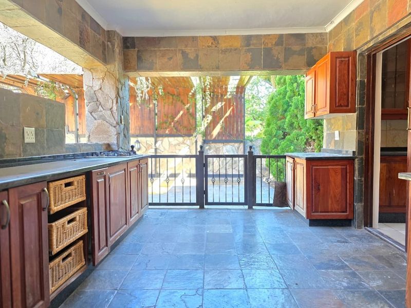 Covered outdoor patio area featuring built-in cabinetry, granite countertops, a gas hob, and stone tile flooring, ideal for outdoor entertaining.