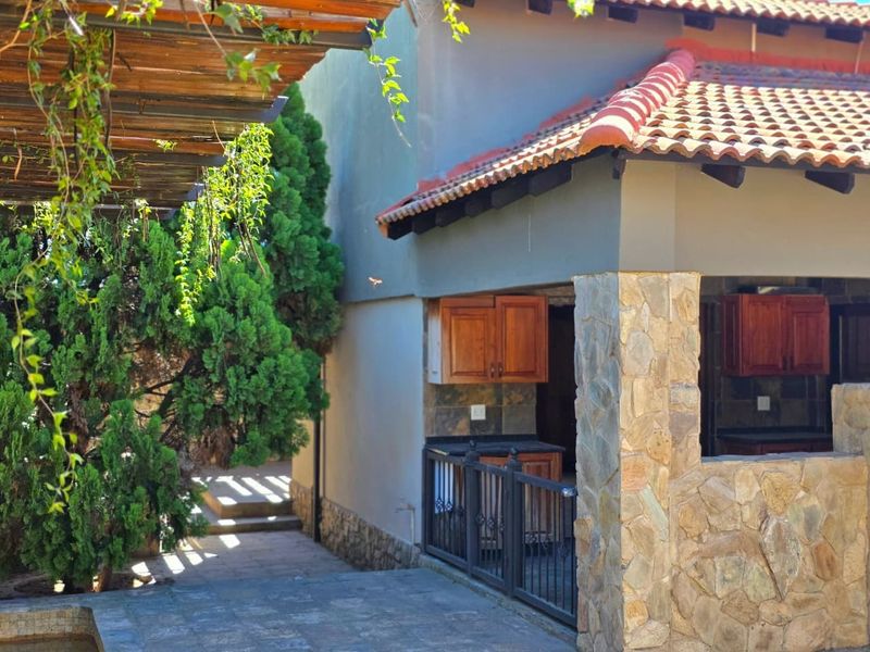 Covered outdoor patio area featuring stone-clad pillars, terracotta roof tiles, and built-in wooden cabinetry, providing a functional space for outdoor entertaining.
