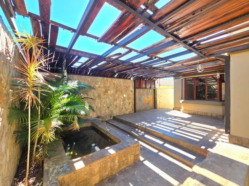 A covered outdoor patio area featuring stone wall cladding, a built-in water feature, and a timber pergola structure.