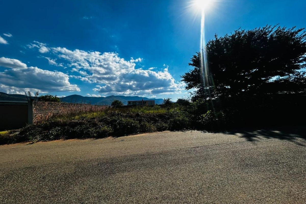 Street view of a vacant residential plot featuring a brick boundary wall with electric fencing and mountain views in the background.