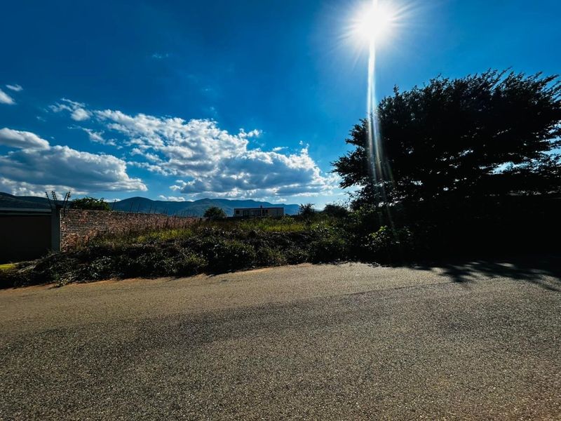 Street view of a vacant residential plot featuring a brick boundary wall with electric fencing and mountain views in the background.