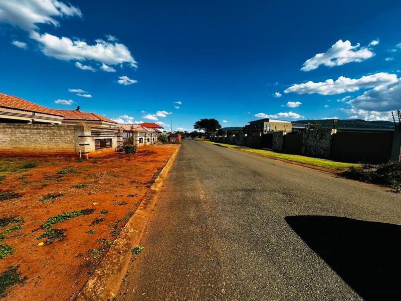 A street view of a residential area featuring paved roads, perimeter walls, and electric fencing under a clear blue sky.