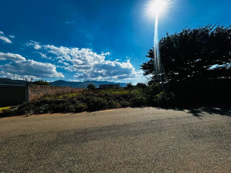 Street view of a vacant residential plot featuring a brick boundary wall with electric fencing and mountain views in the background.