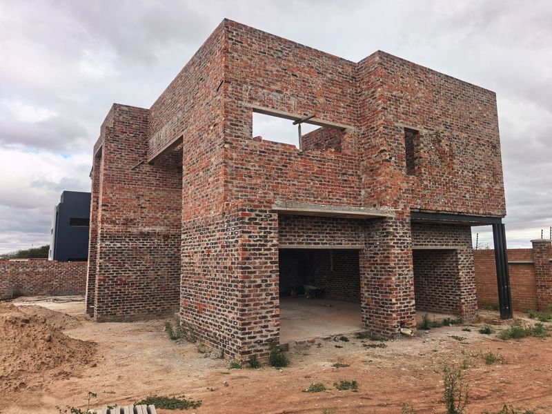 A double-story residential property currently under construction, featuring exposed brickwork and structural steel beams, awaiting completion of finishes and exterior installations.