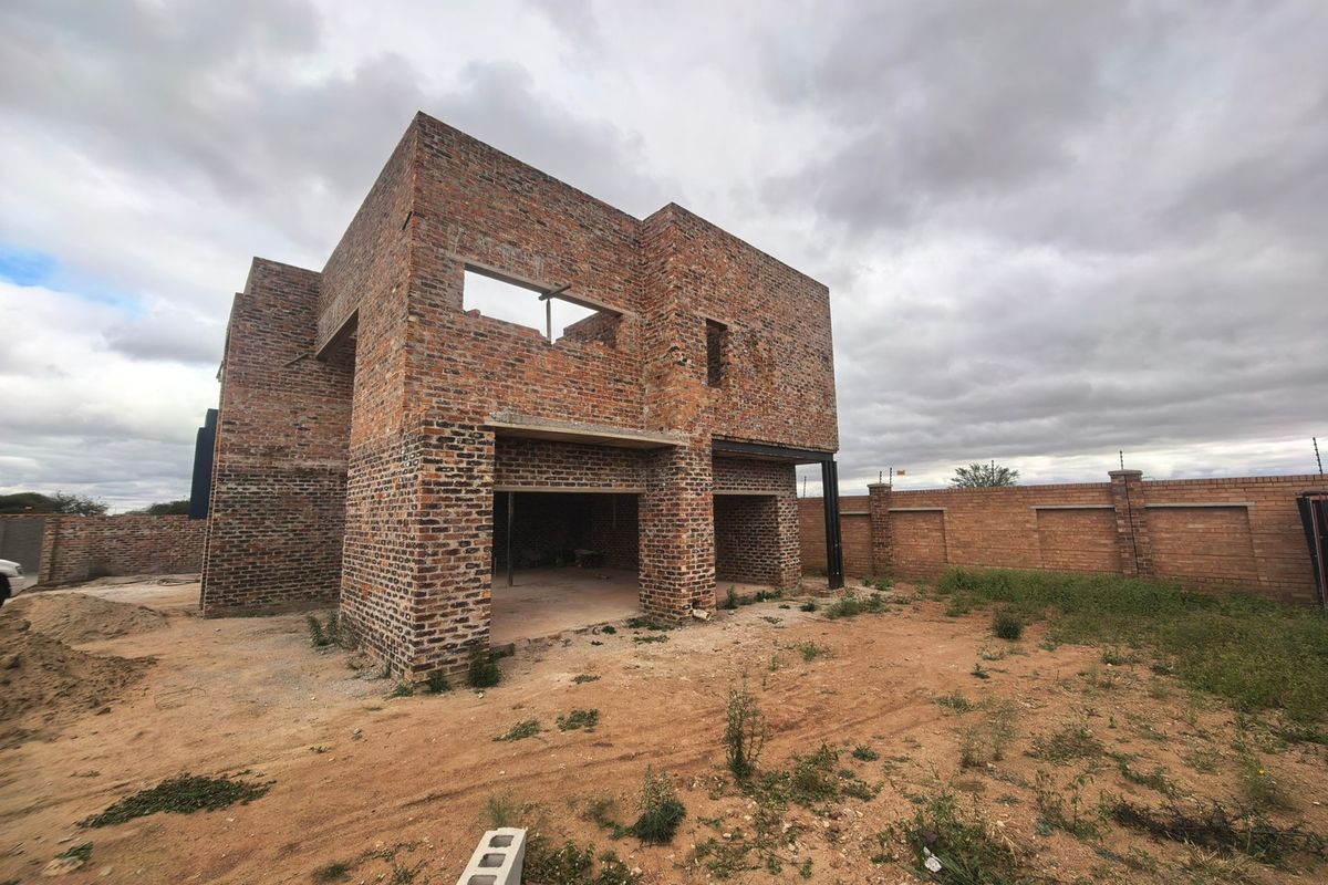A double-story residential property under construction, featuring exposed brickwork, structural steel beams, and an unfinished exterior shell on a large plot.