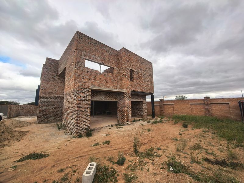 A double-story residential property under construction, featuring exposed brickwork, structural steel beams, and an unfinished exterior shell on a large plot.