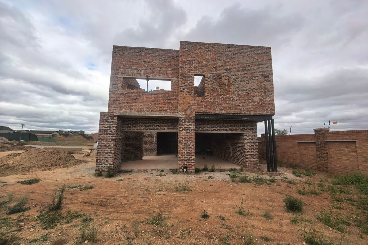 A double-story residential property currently under construction, featuring an exposed brick facade and structural steel supports on a large, undeveloped plot.