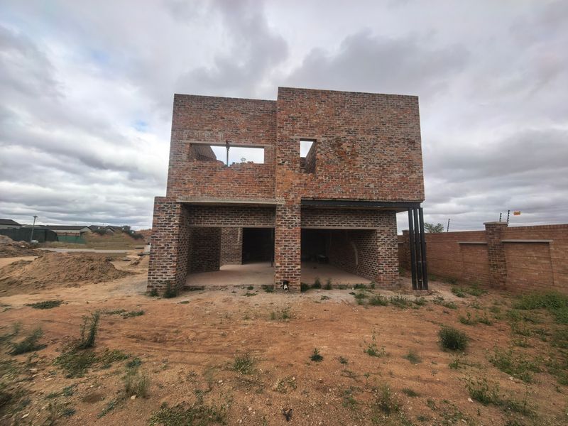 A double-story residential property currently under construction, featuring an exposed brick facade and structural steel supports on a large, undeveloped plot.