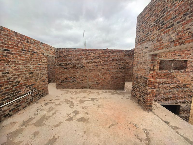 An unfinished interior space under construction featuring exposed brick walls and a raw concrete floor slab.