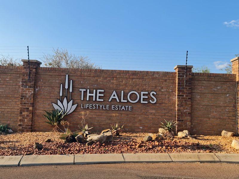 The entrance signage and brick boundary wall of The Aloes Lifestyle Estate, featuring integrated electric fencing and established garden landscaping.
