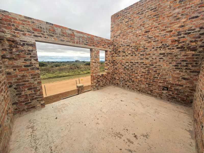 An unfinished bedroom space under construction featuring exposed brick walls, concrete flooring, and a large opening with views of the surrounding landscape.