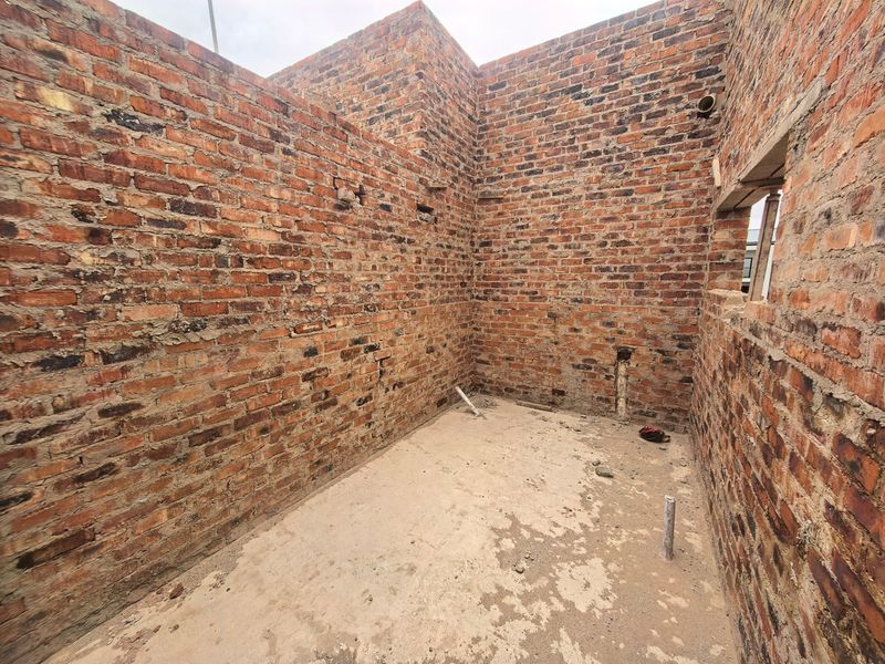 An unfinished utility space featuring exposed brick walls, concrete flooring, and visible plumbing rough-ins, ready for final interior finishes and installation.