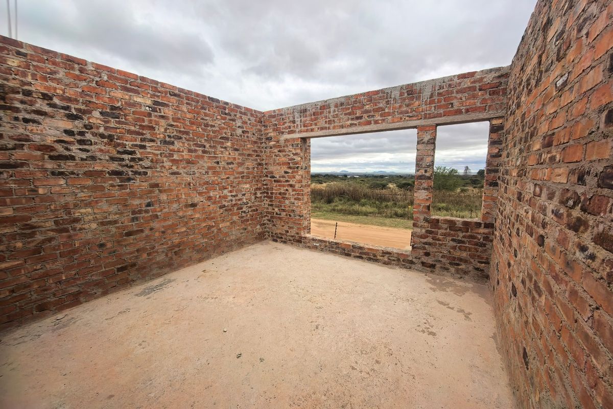An unfinished room under construction featuring exposed brick walls and a concrete floor, offering a view of the surrounding landscape.