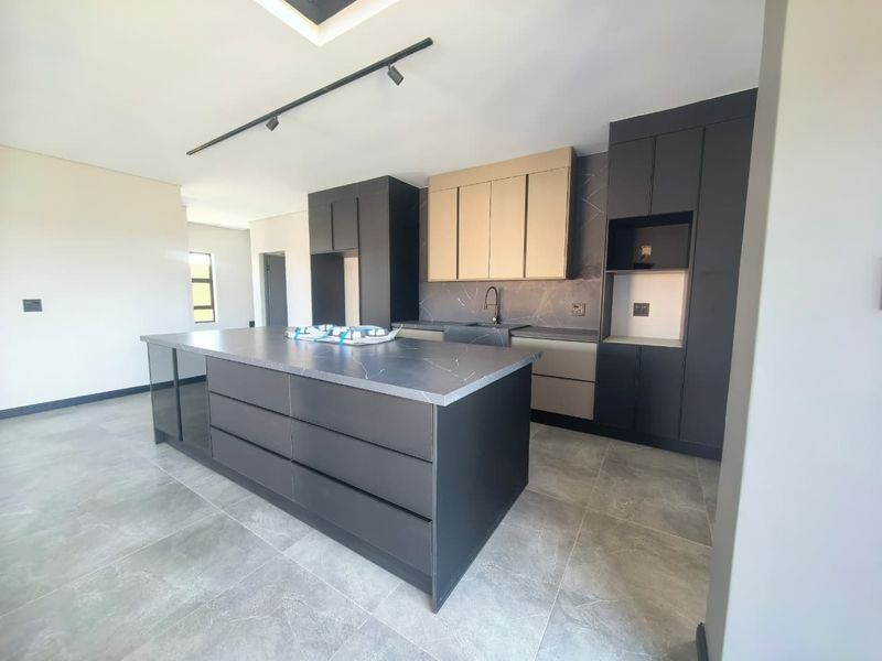 Modern kitchen featuring a large central island, sleek matte cabinetry, stone countertops, and high-quality tiled flooring in a contemporary open-plan layout.