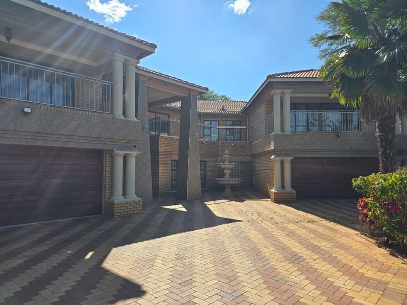 Spacious front exterior featuring a large paved driveway, double garages, decorative stone fountain, and upper-level balconies with brick facade detailing.