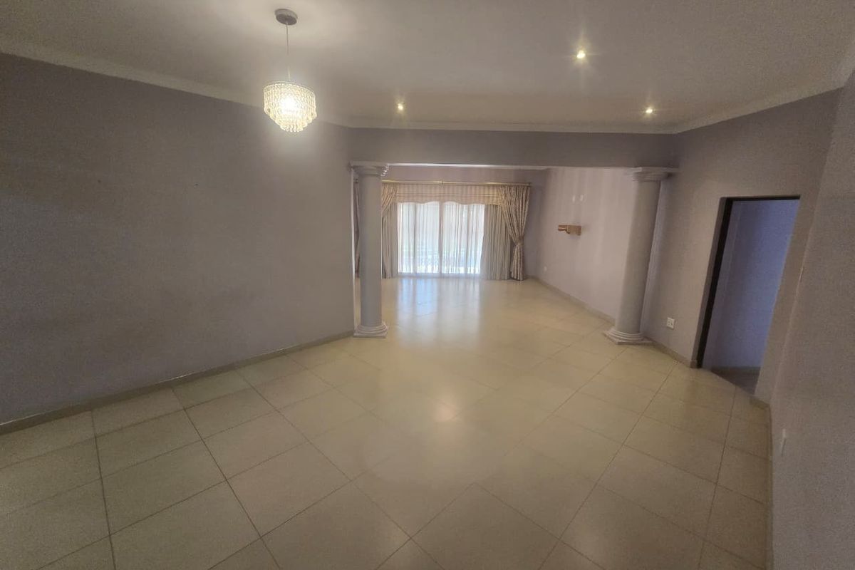 Spacious open-plan living area featuring neutral tiled flooring, decorative columns, and sliding glass doors leading to an outdoor space.