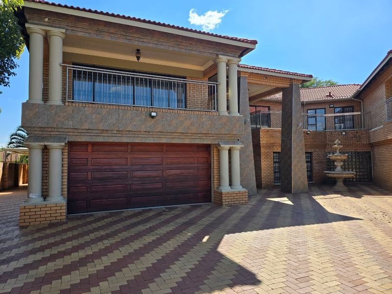 Front elevation of a multi-story residence featuring a double garage, stone-clad pillars, a balcony with stainless steel railing, and a decorative water fountain.