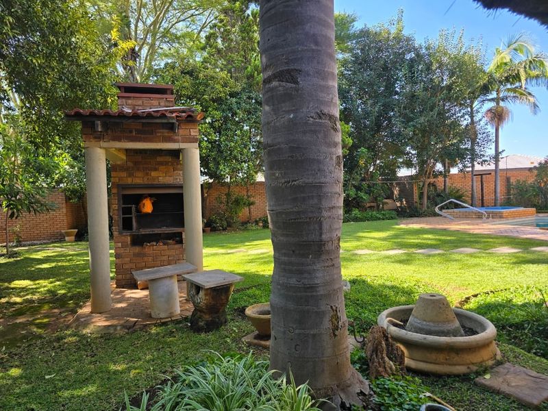 Spacious garden featuring a built-in brick braai area, a swimming pool, and established landscaping with mature trees and a stone fountain.