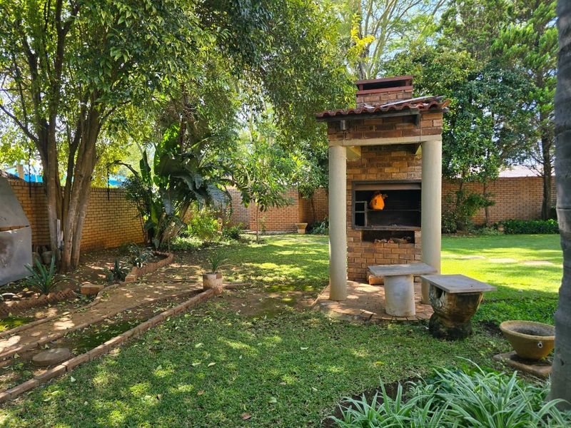 A lush garden area featuring a substantial brick built-in braai, concrete seating, and mature trees, providing a private outdoor entertainment space.
