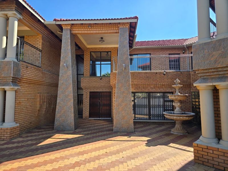 Spacious rear courtyard featuring a brick facade, stone-clad pillars, a balcony with stainless steel railings, and a decorative stone fountain.