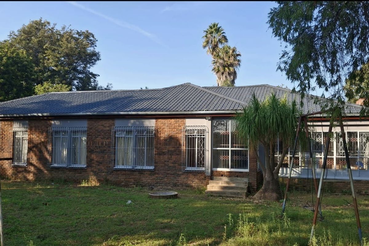 Rear view of a single-story brick house featuring a tiled roof, security bars on windows, and a small concrete entrance step.