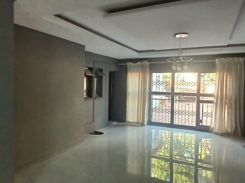 Spacious living area featuring neutral grey walls, polished tiled flooring, recessed ceiling details, and a large sliding glass door with integrated security gate.