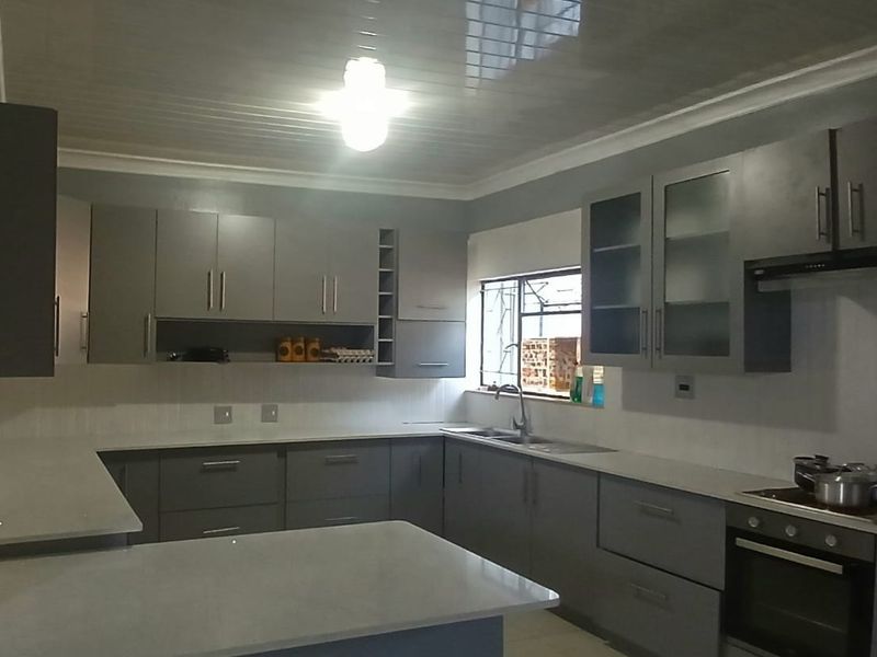 Modern kitchen featuring grey built-in cabinetry, stone countertops, a tiled backsplash, and integrated appliances including an oven and extractor fan.