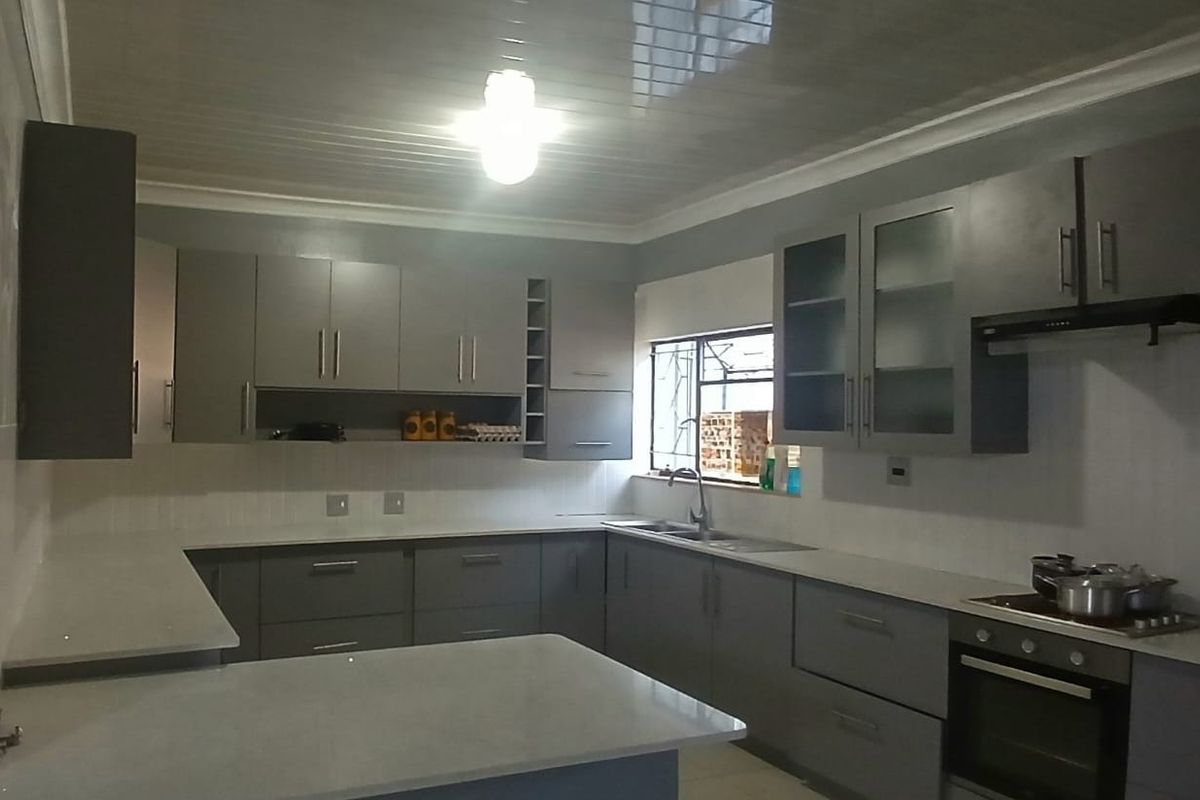 Modern kitchen featuring grey built-in cabinetry, stone countertops, a tiled backsplash, and integrated appliances including an oven and extractor fan.