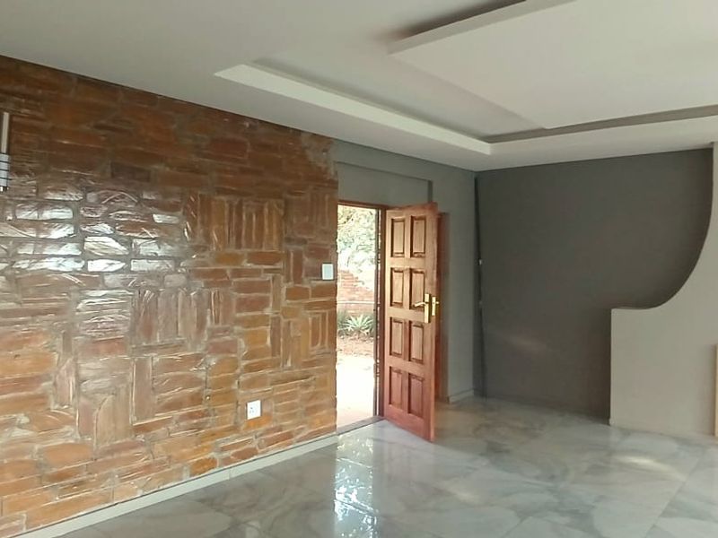 Spacious living room featuring a striking exposed brick feature wall, modern fireplace surround, recessed ceiling detail, and polished marble-look floor tiles.