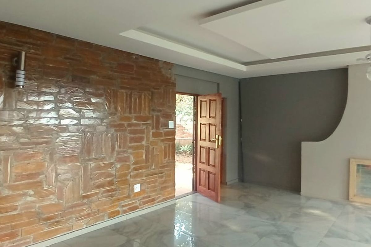 Spacious living room featuring a striking exposed brick feature wall, modern fireplace surround, recessed ceiling detail, and polished marble-look floor tiles.