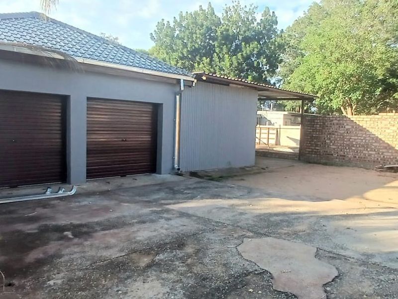 Exterior view of a double garage with a concrete driveway and brick boundary wall, showing signs of wear and weathering.