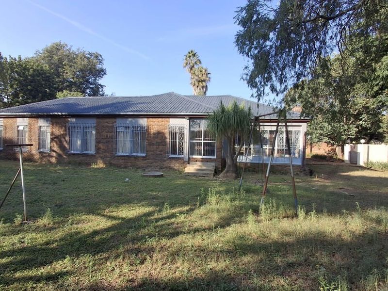 Rear view of a single-story brick house featuring a tiled roof, security bars on windows, and a spacious backyard area.