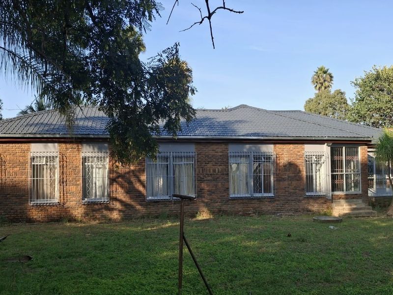 Rear view of a single-story face brick house featuring a tiled roof and security bars on windows, set within a spacious garden.