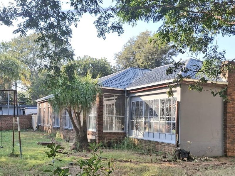 Rear view of the house featuring a brick chimney, tiled roof, and security-barred windows, set within a large, overgrown garden area.