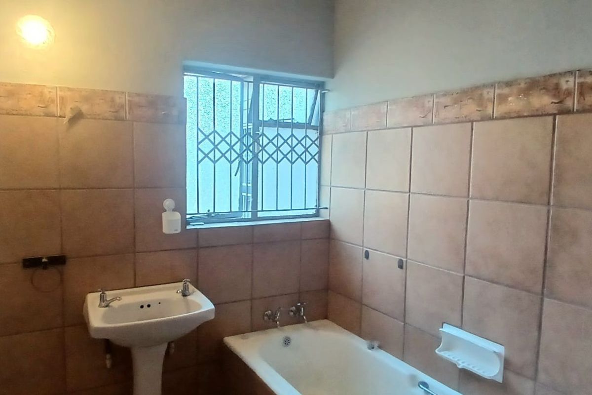 A functional bathroom featuring a pedestal washbasin, a standard bathtub, and full-height ceramic wall tiling with a security gate on the window.