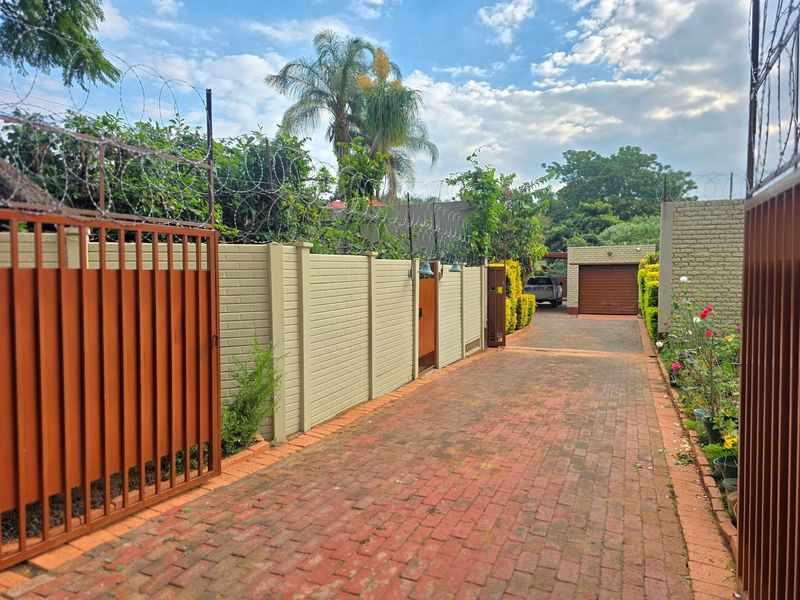 A secure residential entrance featuring a paved brick driveway, perimeter precast walling with razor wire security, and a private garage.